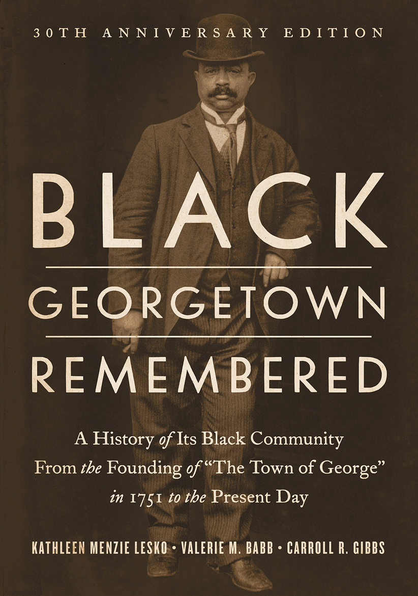 A photograph of the bookcover of Black Georgetown Remembered. The cover consists of a circa 1920s black and white photograph of African American businessman George Martin standing in front of the Blue Moon Theatre, Georgetown, Washington DC. Superimposed on the picture is the title, Black Georgetown Remembered: A History of Its Black Community from the Founding of "The Town of George" in 1751 to the Present Day. Authors names appear below.