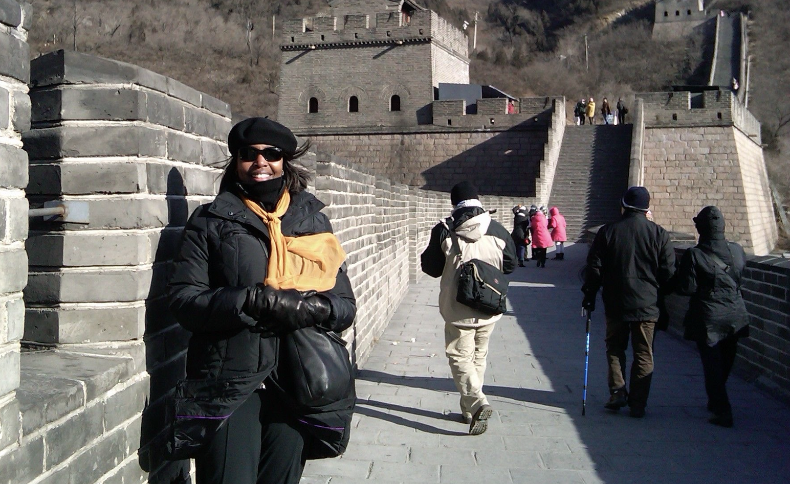 Photograph of Valerie Babb in winter coast and beret standing in front of the entry steps to the Great Wall of China. The day is cold and blustery.